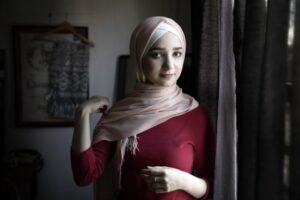Sedra Al-Yousef retter på sin hijab mens hun står i en stue