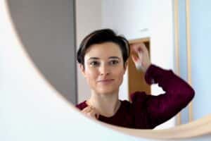 Karen Melchior pale faced woman with a purple shirt on looking into a mirror adjusting her short dark har.